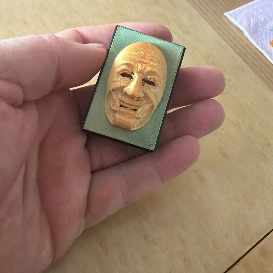 Miniatur einer Maske als Plakette in der Hand